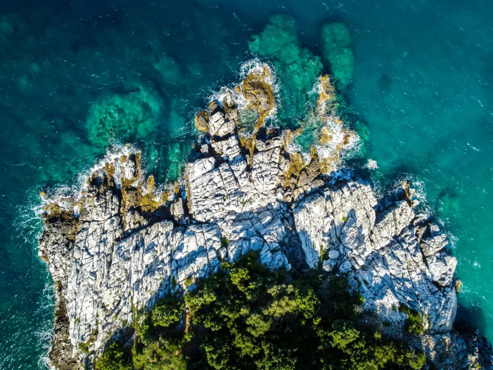 Stunning aerial shot of a rocky coastline in Greece with vibrant turquoise waters, showcasing natural beauty.