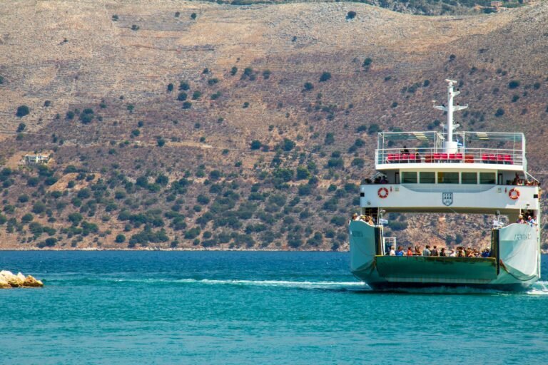 Ferry carrying passengers across the clear blue Ionian Sea in Greece, with rugged hills in the background.